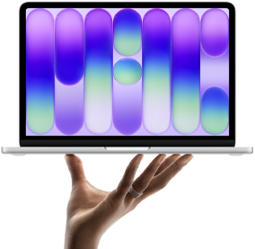 MacBook Neo in silver color, balanced on fingertips of open hand, screen displaying colorful abstract pattern