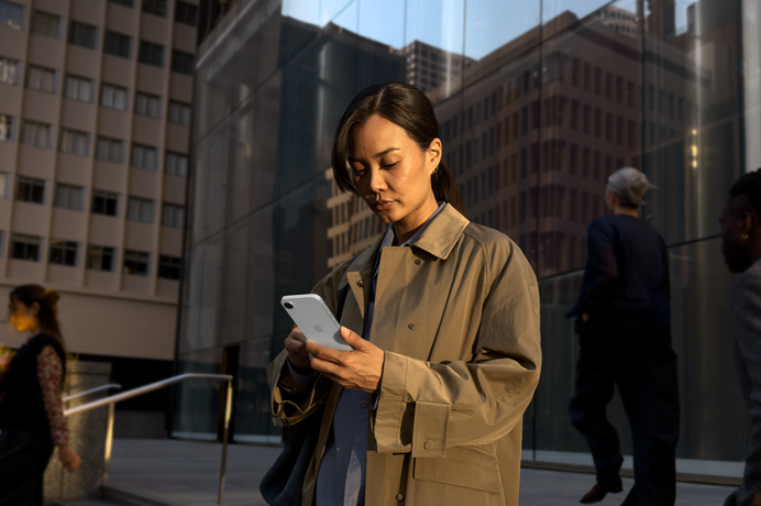 A person using a white iPhone 17e to continue work outside of an office building