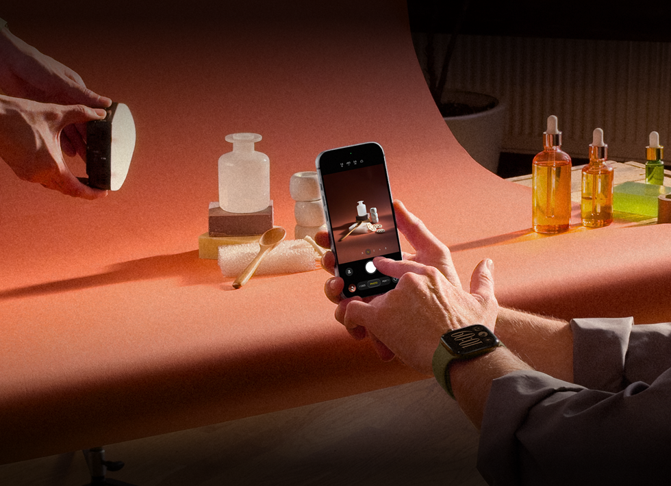 Een fotoshoot op de werkplek, iemand fotografeert met een iPhone producten tegen een achtergrond, iemand houdt een lamp vast