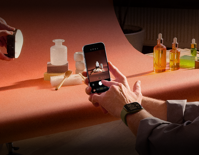 Een fotoshoot op de werkplek, iemand fotografeert met een iPhone producten tegen een achtergrond, iemand houdt een lamp vast