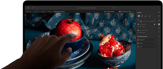 MacBook Pro met PROLED XDR-display met een stilleven van granaatappels met blauw keramiek en textiel, een hand reikt naar het scherm om de creatie aan te raken