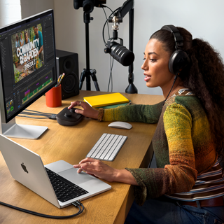 Een vrouw werkt thuis aan haar bureau met een MacBook Pro die is aangesloten op twee externe displays. Ze draagt een koptelefoon en praat in een microfoon